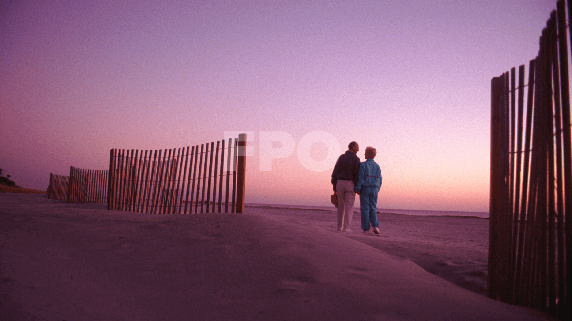 senior couple walking together on the beach at sunset